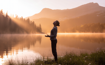 Ruhige Naturszene bei Sonnenaufgang: Eine Person steht an einem nebelverhangenen See und atmet tief durch, umgeben von sanftem goldenem Licht und entspannender Atmosphäre. Stress abbauen in 5 Minuten.