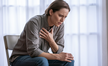 Panik stoppen sofort: Person sitzt und hält sich die Brust bei Herzrasen und Angst, Anzeichen einer Panikreaktion